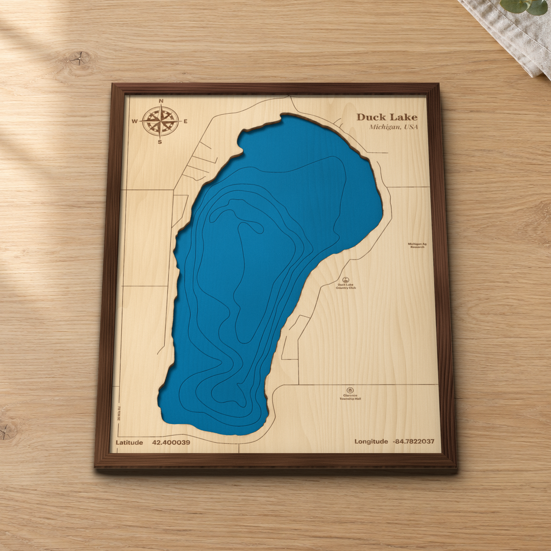 Duck Lake wood map lying flat on a wooden tabletop, showing the depth contours and the roads around the shore engraved in