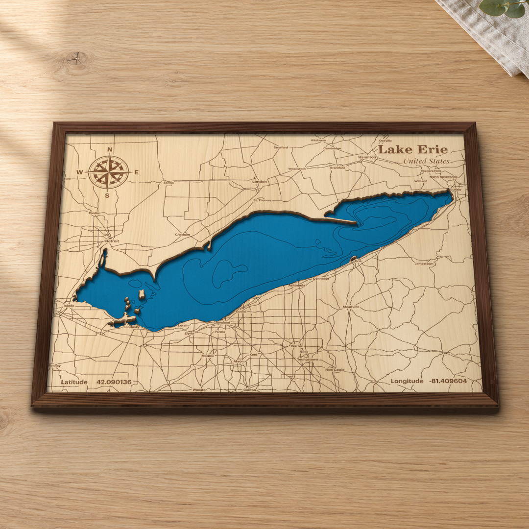 Lake Erie wood map lying flat on a wooden tabletop, showing the whole lake's depth contours and the islands off Sandusky, with engraved cities and highways on the U.S. and Ontario shores