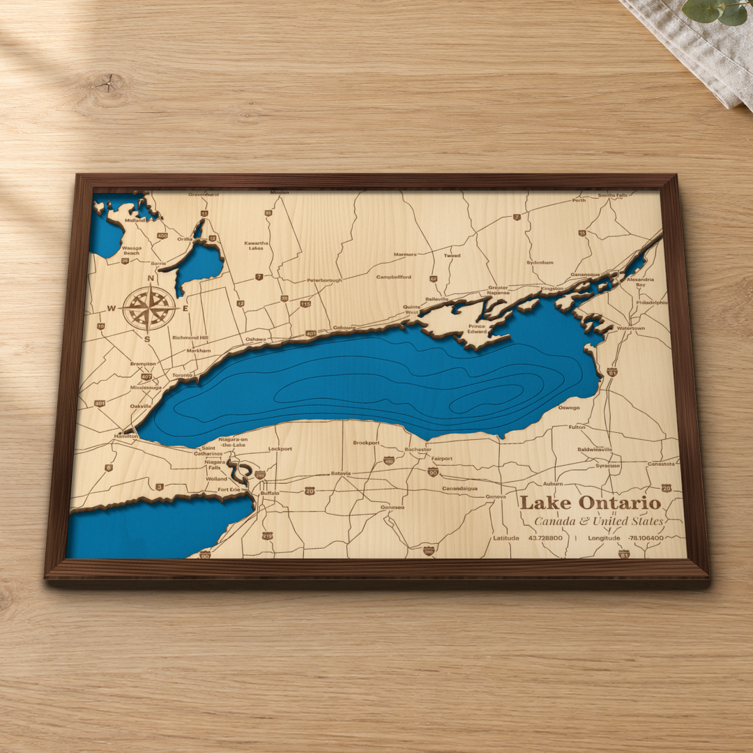 Lake Ontario wood map lying flat on a wooden tabletop, showing the lake's depth contours with engraved cities and highways from Toronto and Niagara to Rochester, Kingston and Watertown