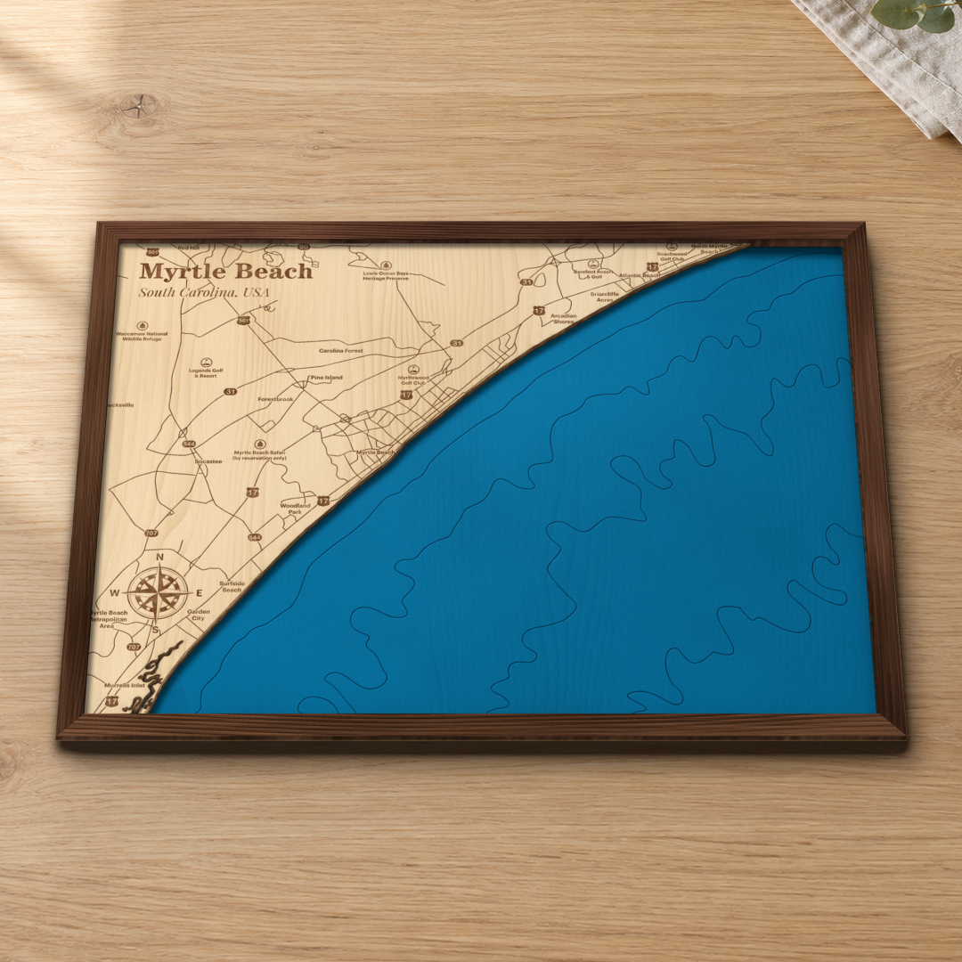 Myrtle Beach wood map lying flat on a wooden tabletop, showing the ocean depth contours and the Grand Strand from North Myrtle Beach to Murrells Inlet engraved in