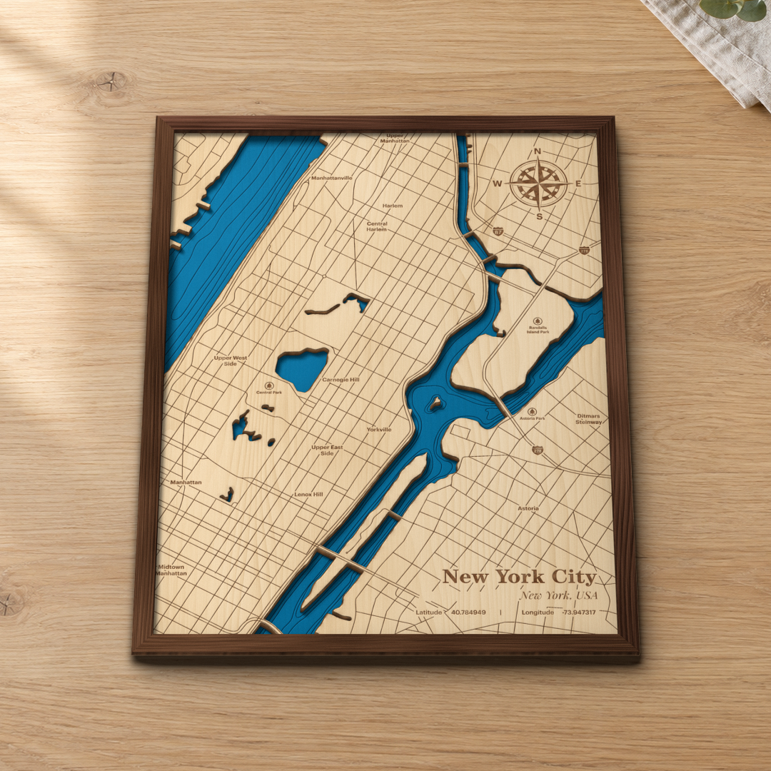 New York City wood map lying flat on a wooden tabletop, showing Central Park, the Hudson and East Rivers and Randalls Island, with engraved neighborhoods from Harlem to Astoria