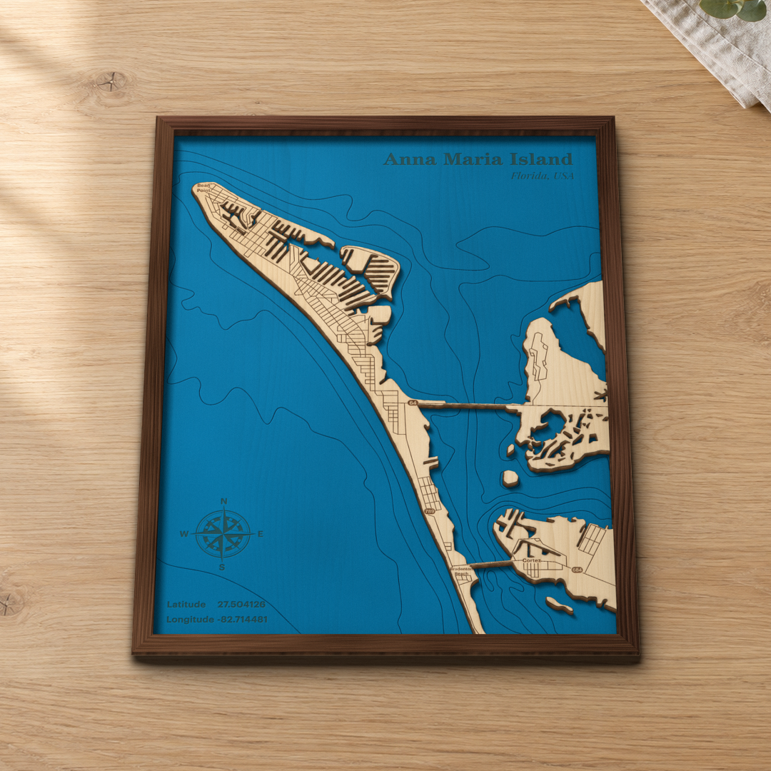 Anna Maria Island wood map lying flat on a wooden tabletop, showing the Gulf depth contours, the canals and the bridges to the mainland engraved in