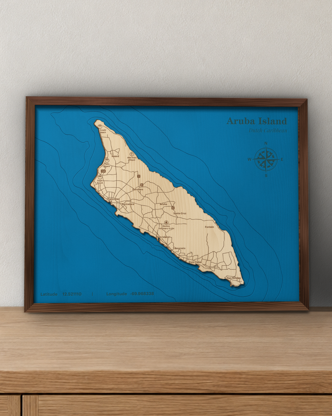Aruba wood map in a walnut frame standing on a wooden sideboard against a wall for scale