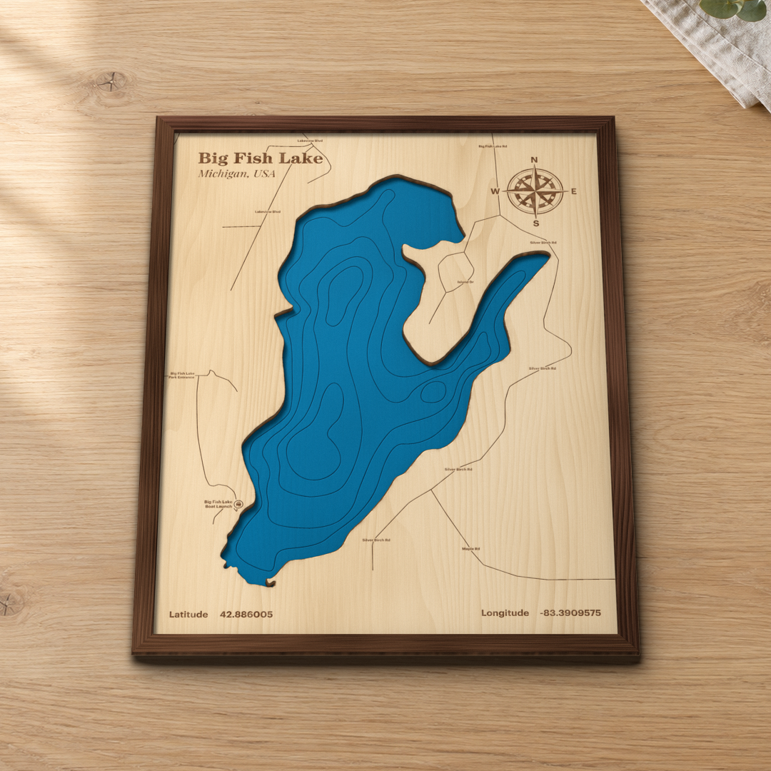 Big Fish Lake wood map lying flat on a wooden tabletop, showing the depth contours and the roads around the bays engraved in