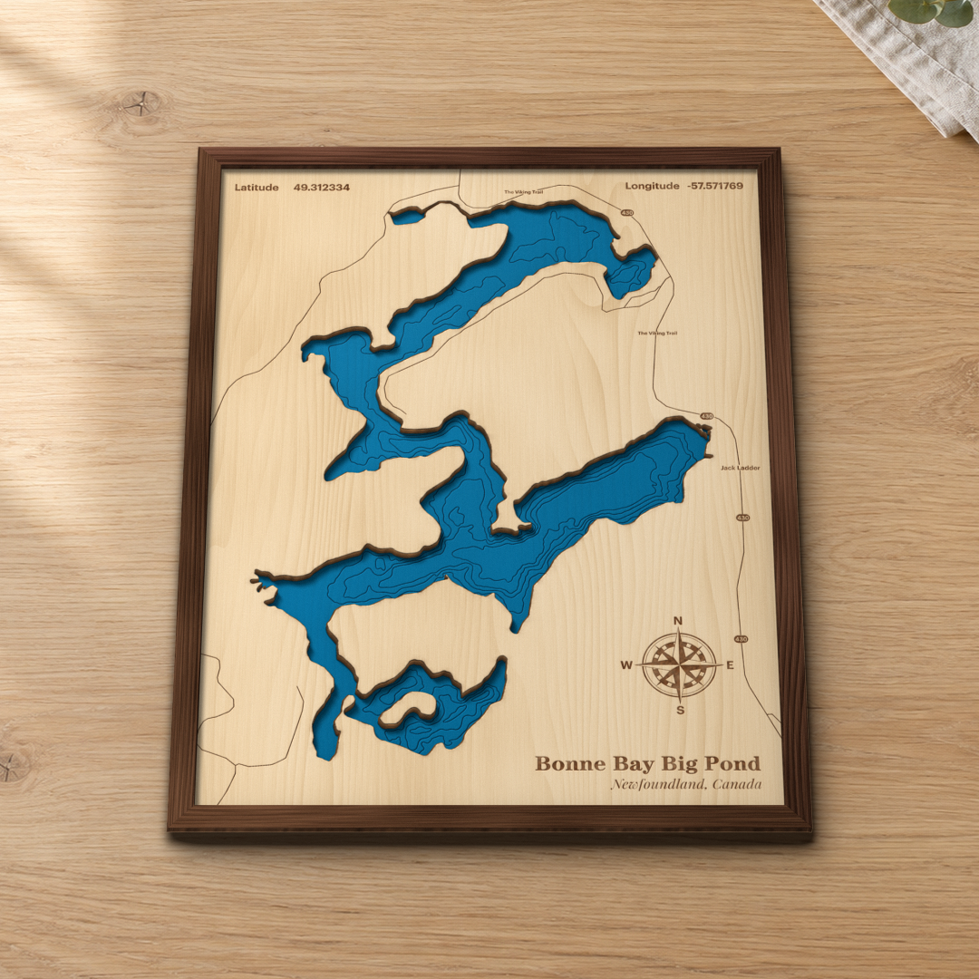 Bonne Bay Big Pond wood map lying flat on a wooden tabletop, showing the pond's long arms and depth contours with the Viking Trail (Route 430) engraved in