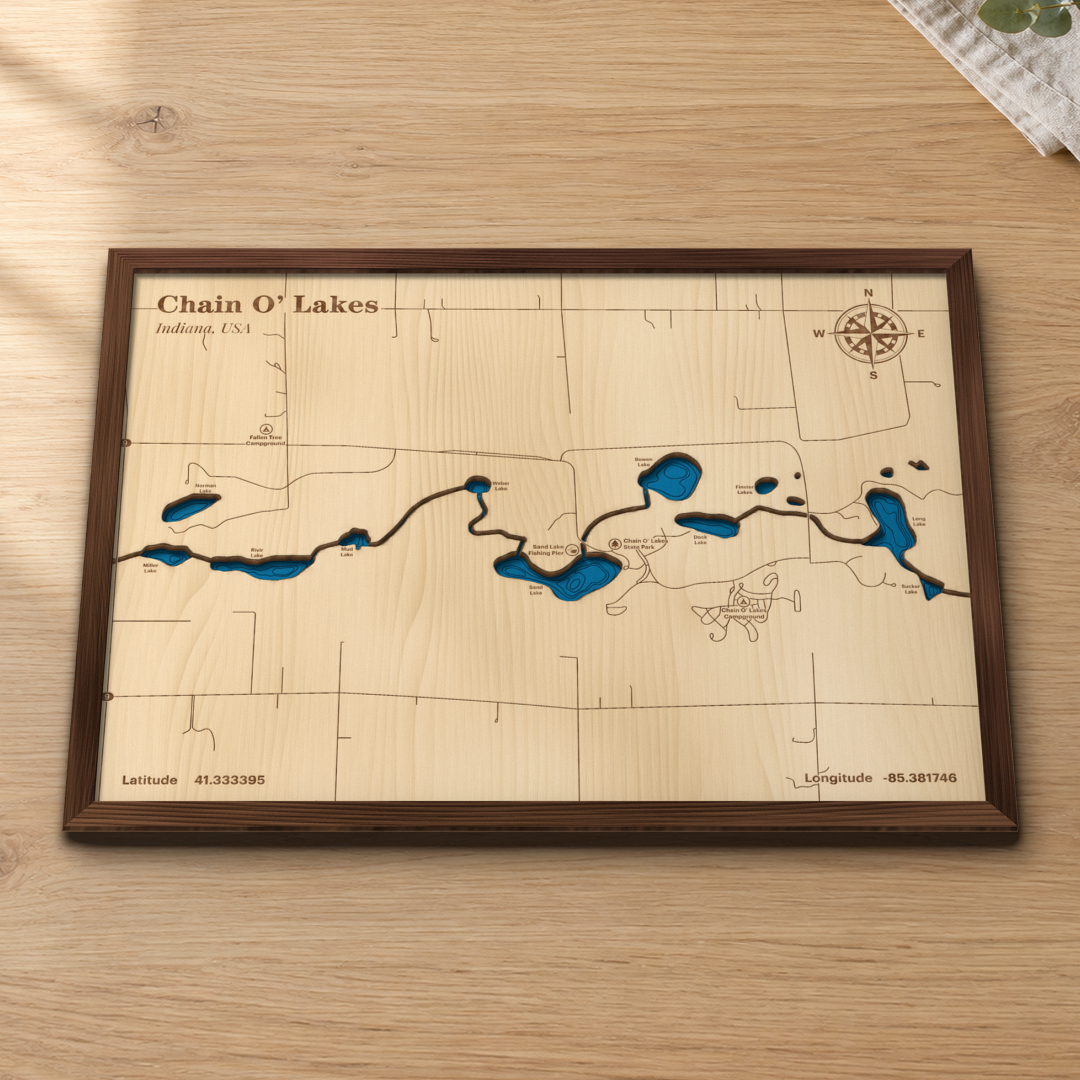 Chain O' Lakes wood map lying flat on a wooden tabletop, showing the nine connected kettle lakes and their depth contours engraved in