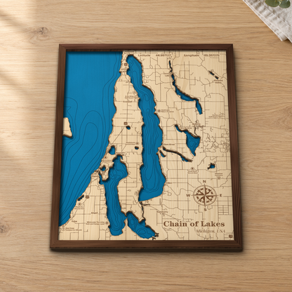 Chain of Lakes wood map lying flat on a wooden tabletop, showing the chain's depth contours from Torch Lake to Elk Rapids, with engraved towns, preserves and highways