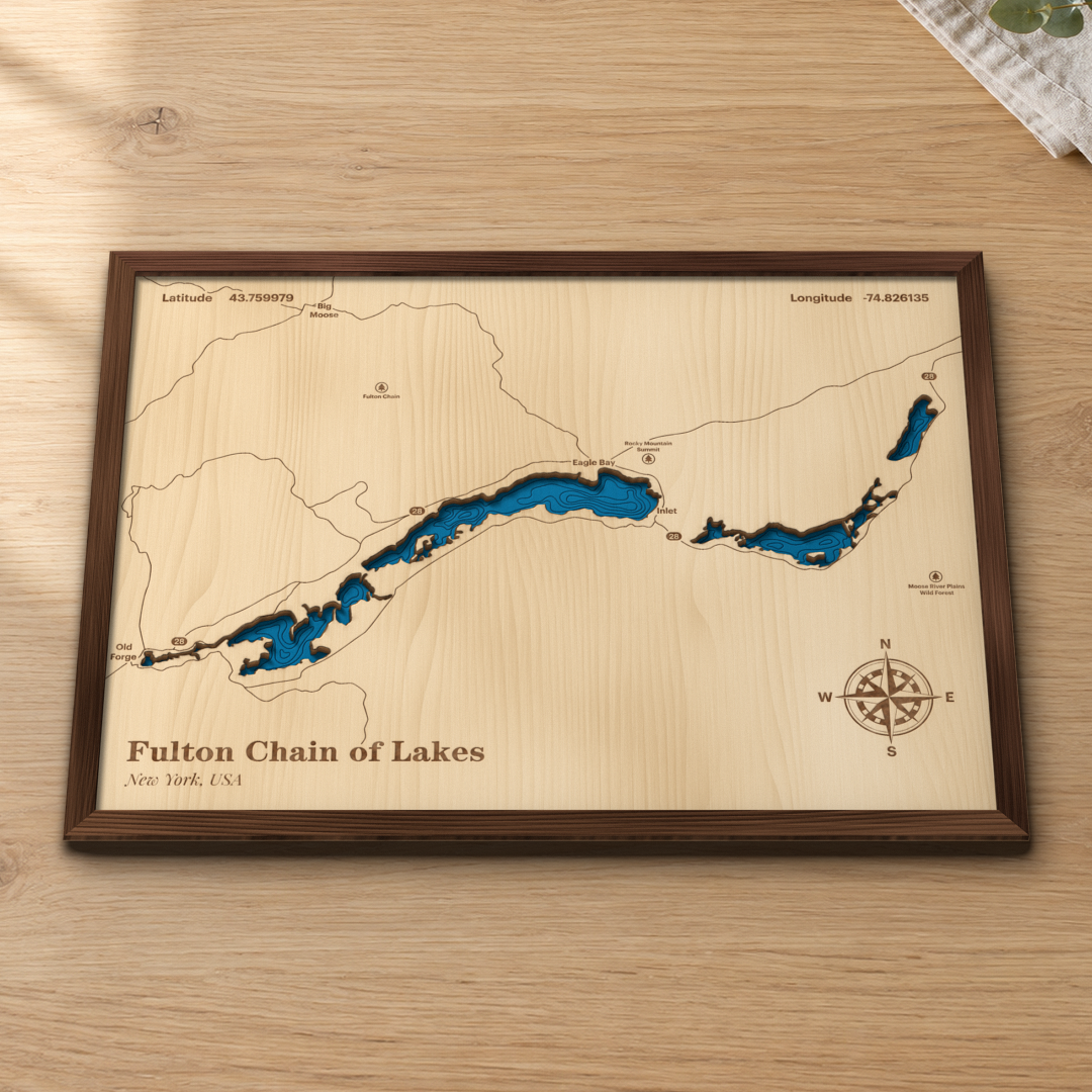 Fulton Chain of Lakes wood map lying flat on a wooden tabletop, showing the chain's depth contours from Old Forge past Eagle Bay to Inlet along Route 28