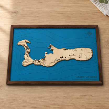 Grand Cayman wood map lying flat on a wooden tabletop, showing the whole island, the North Sound and offshore depth contours, with engraved towns and beaches from West Bay to the East End