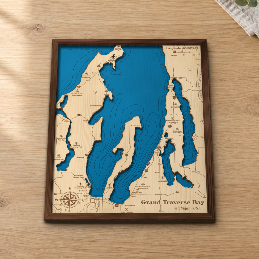 Grand Traverse Bay wood map lying flat on a wooden tabletop, showing the depth contours, Old Mission Peninsula and Traverse City engraved in