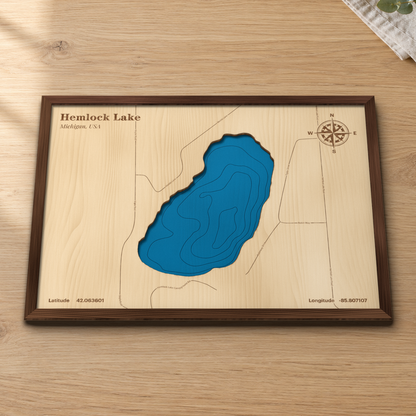 Hemlock Lake wood map lying flat on a wooden tabletop, showing the lake's deep contours with engraved roads including Hemlock Lake Campground Rd and Robinway Drive