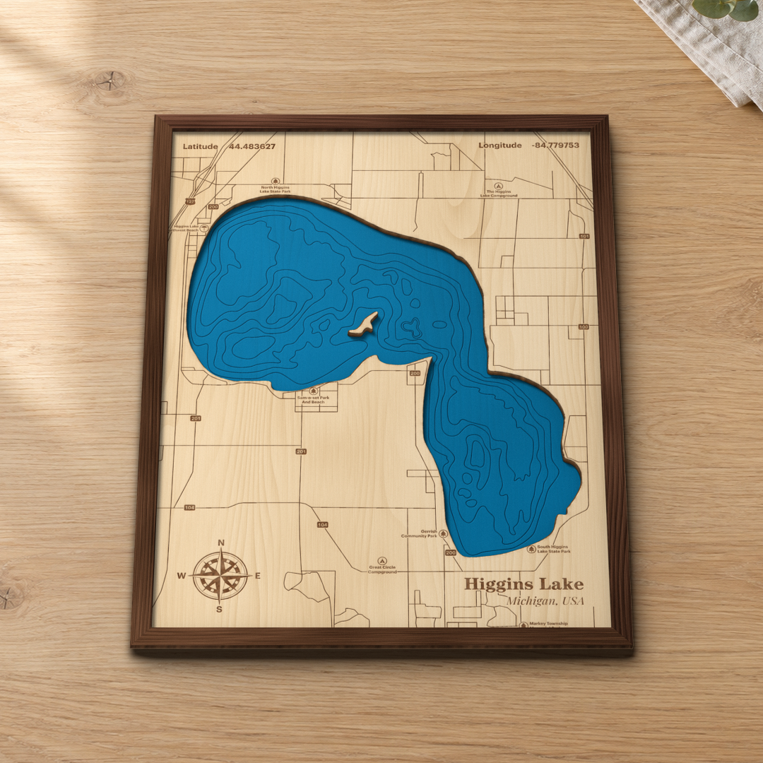 Higgins Lake wood map lying flat on a wooden tabletop, showing the depth contours and the famous drop-offs engraved in