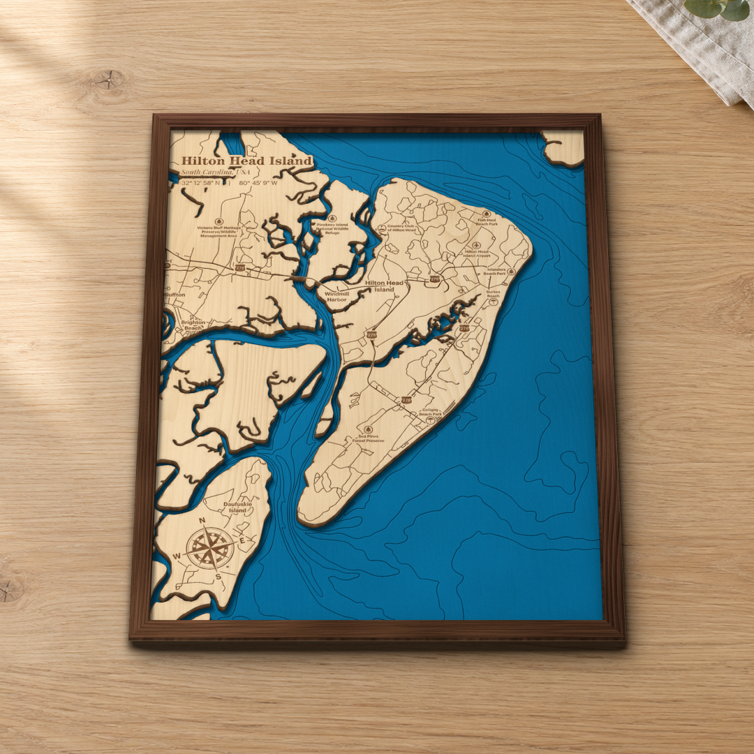Hilton Head Island wood map lying flat on a wooden tabletop, showing the island's marsh creeks and offshore depth contours, with Bluffton and Daufuskie Island across the water