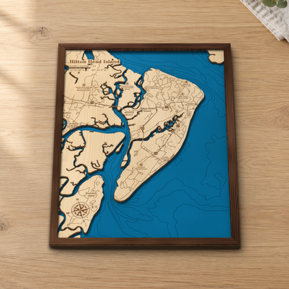 Hilton Head Island wood map lying flat on a wooden tabletop, showing the island's marsh creeks and offshore depth contours, with Bluffton and Daufuskie Island across the water