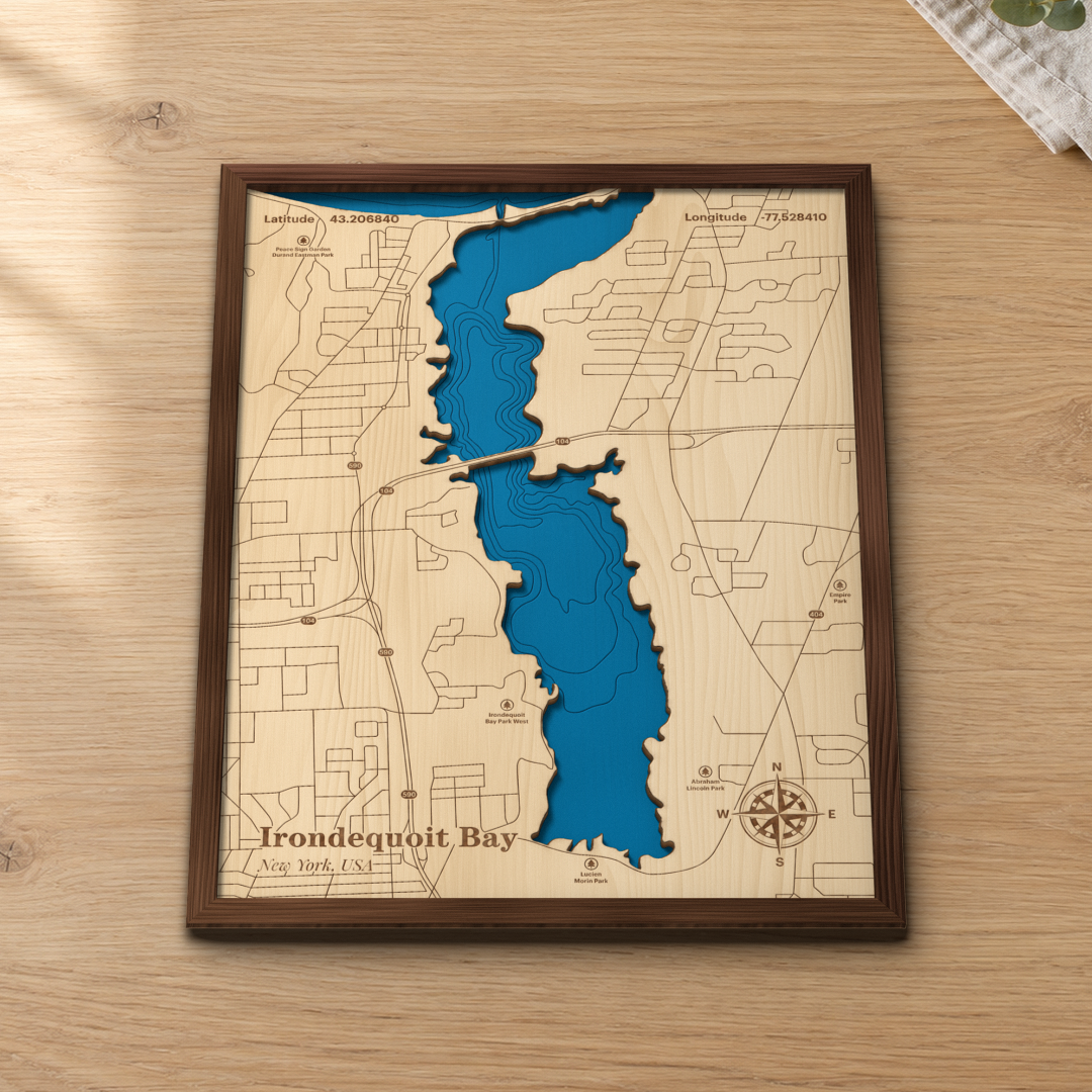 Irondequoit Bay wood map lying flat on a wooden tabletop, showing the bay's depth contours from Lake Ontario to Lucien Morin Park, with engraved parks and roads