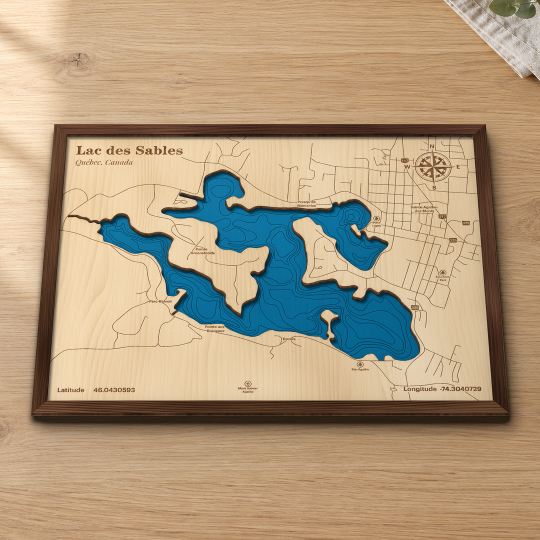 Lac des Sables wood map lying flat on a wooden tabletop, showing the lake's depth contours with Sainte-Agathe-des-Monts, Parc-Belvoir and the points around the shore engraved in
