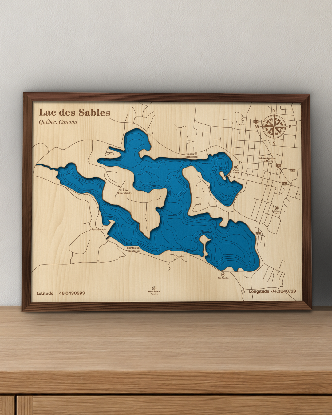 Lac des Sables wood map in a walnut frame standing on a wooden sideboard against a wall for scale