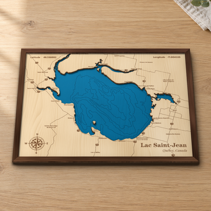 Lac Saint-Jean wood map lying flat on a wooden tabletop, showing the lake's depth contours with Roberval, Alma, Péribonka and the shoreline towns engraved in