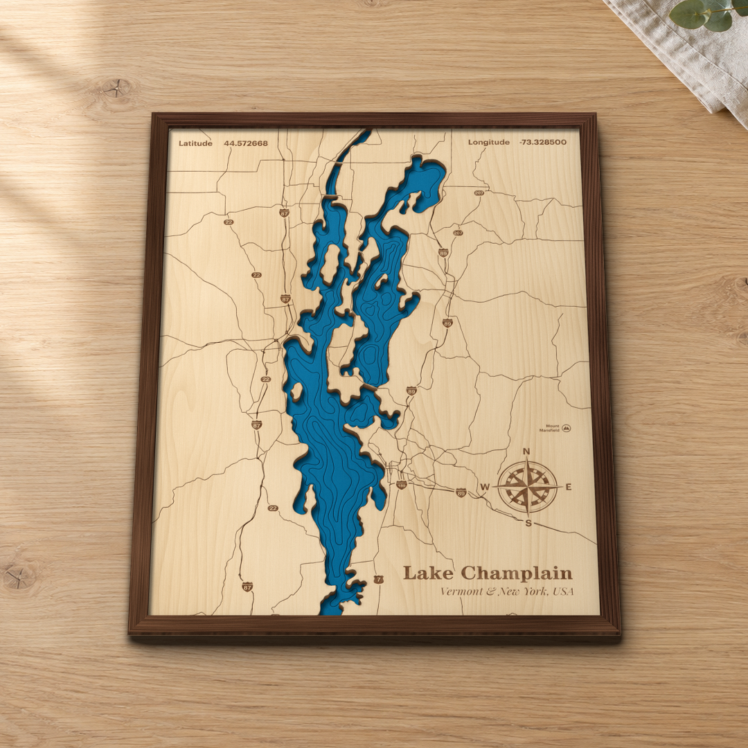 Lake Champlain wood map lying flat on a wooden tabletop, showing the lake's depth contours, the Champlain Islands and Mount Mansfield engraved in