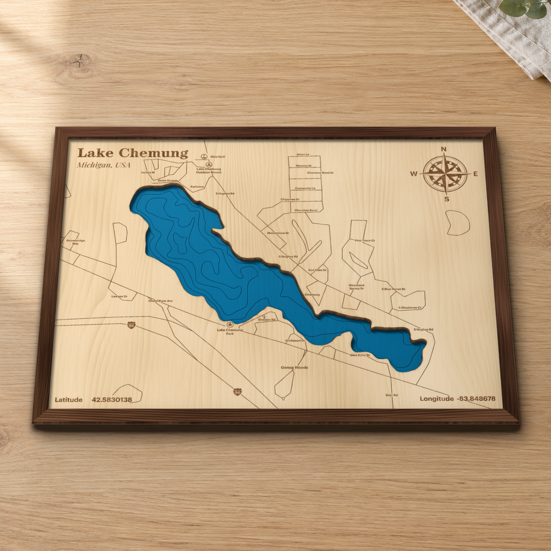 Lake Chemung wood map lying flat on a wooden tabletop, showing the lake's depth contours with Lake Chemung Park, S Hughes Rd and Grand River Ave engraved in