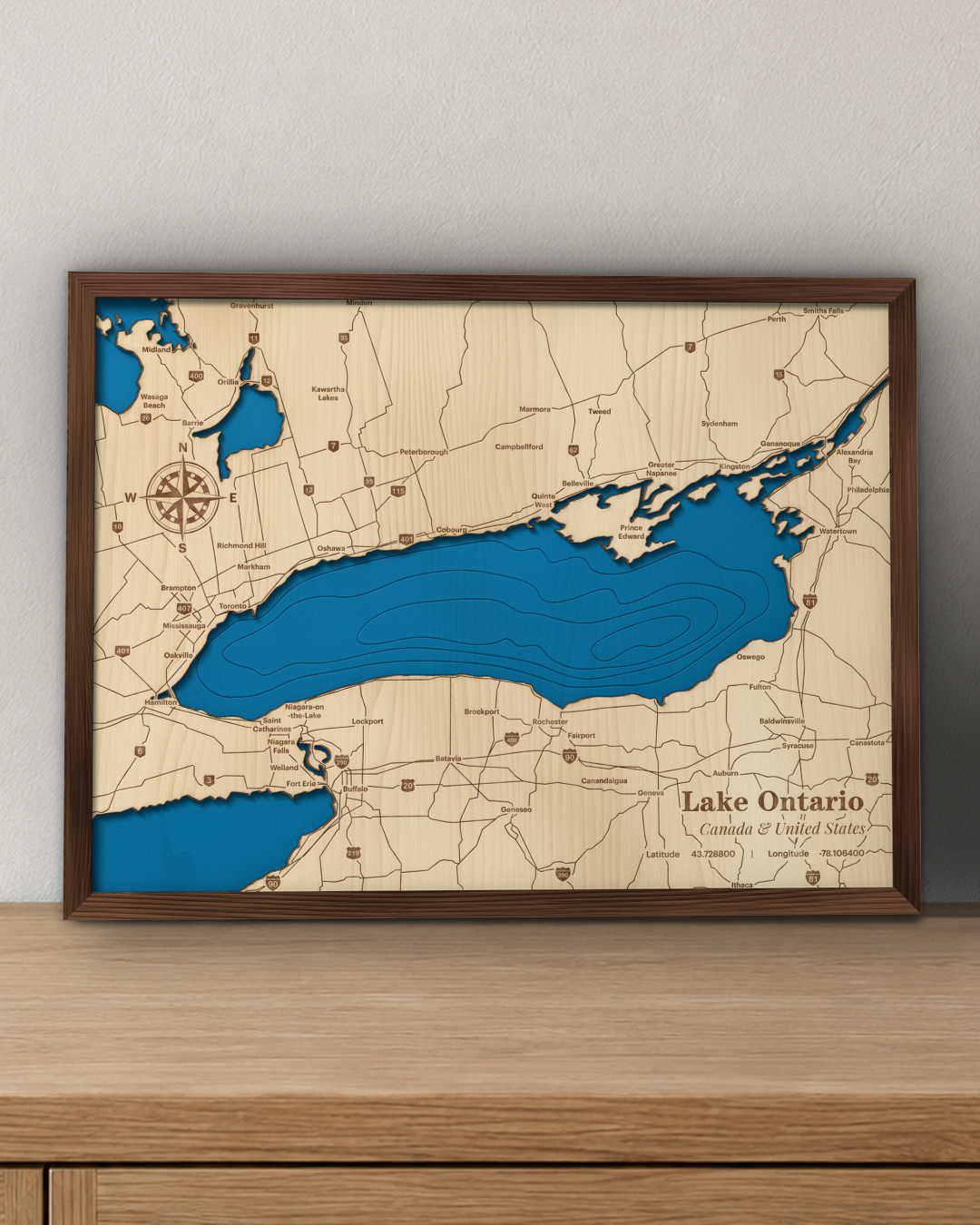 Lake Ontario wood map in a walnut frame standing on a wooden sideboard against a wall for scale