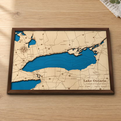 Lake Ontario wood map lying flat on a wooden tabletop, showing the lake's depth contours with engraved cities and highways from Toronto and Niagara to Rochester, Kingston and Watertown