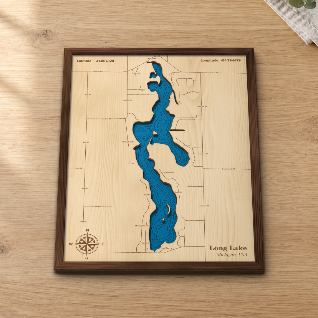 Long Lake wood map lying flat on a wooden tabletop, showing the lake's depth contours with the lanes and roads around its shoreline engraved in