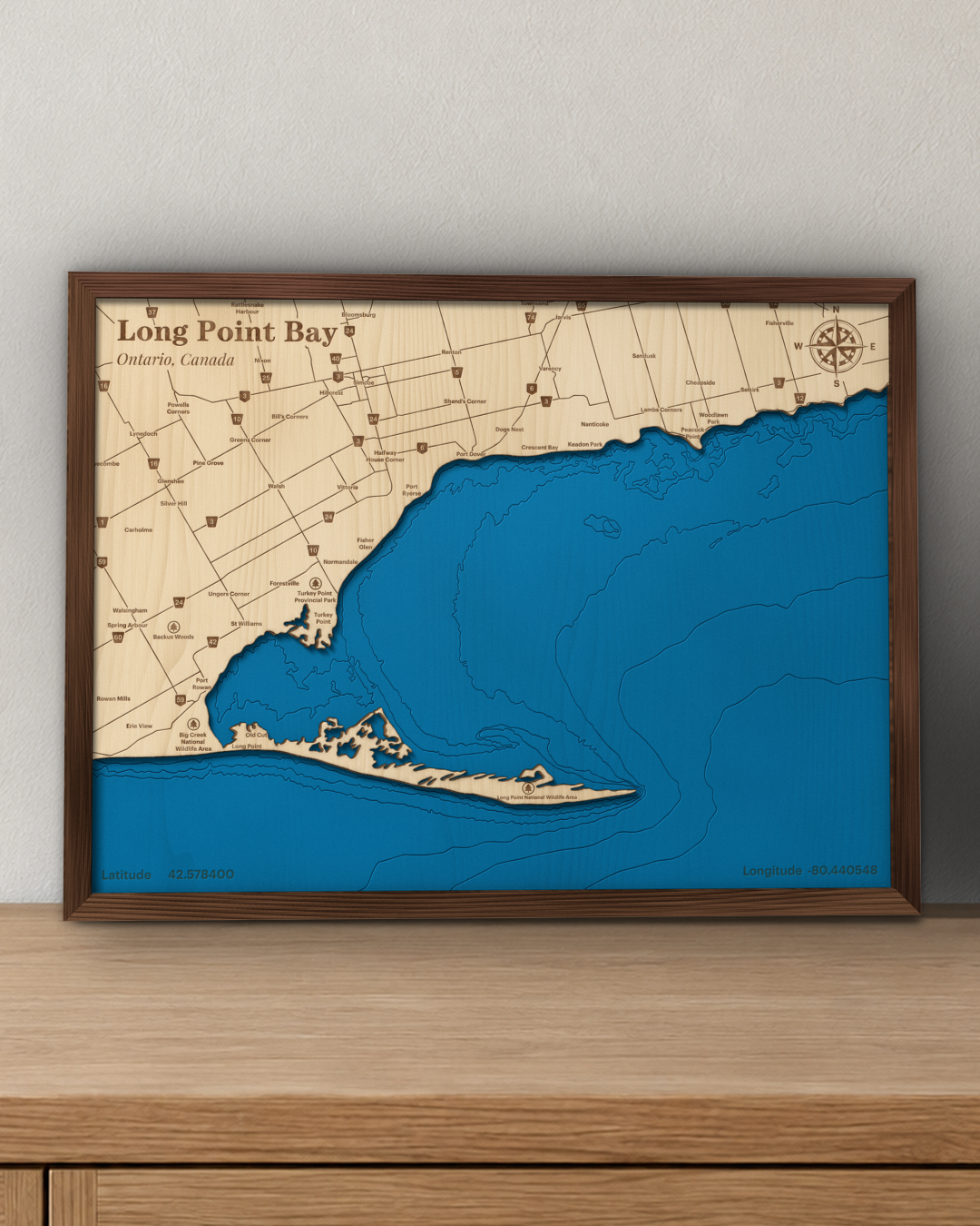 Long Point Bay wood map in a walnut frame standing on a wooden sideboard against a wall for scale