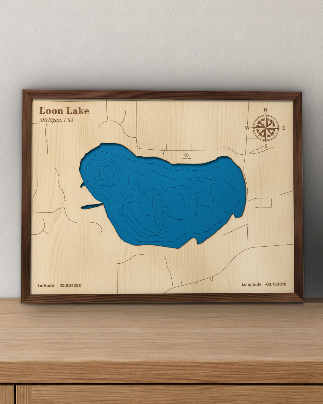 Loon Lake wood map in a walnut frame standing on a wooden sideboard against a wall for scale