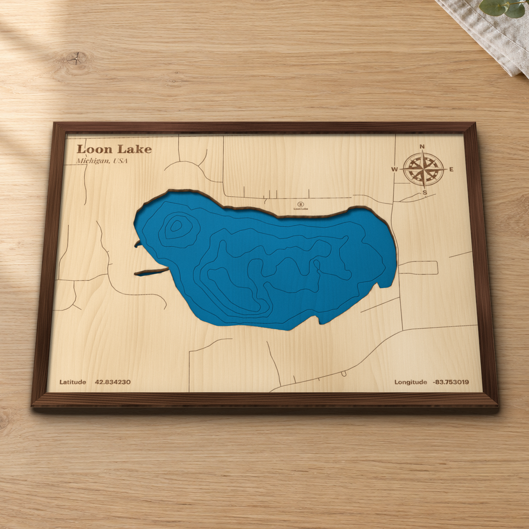 Loon Lake wood map lying flat on a wooden tabletop, showing the lake's depth contours and the roads around its shore
