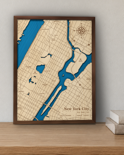 New York City wood map in a walnut frame standing on a wooden shelf against a wall beside a stack of books for scale