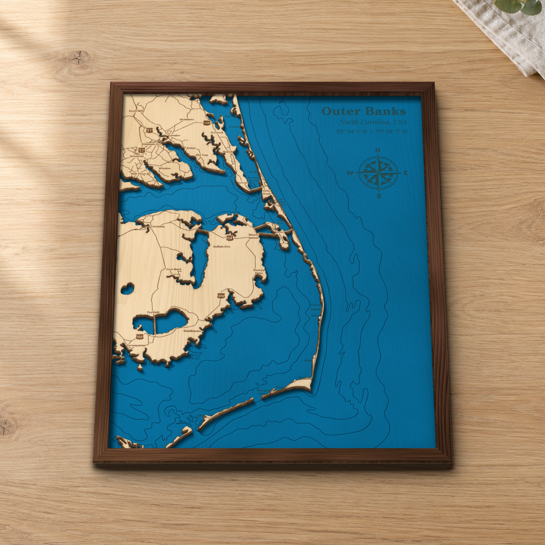 Outer Banks wood map lying flat on a wooden tabletop, showing the barrier islands, Roanoke Island and the depth contours of the sounds and the Atlantic