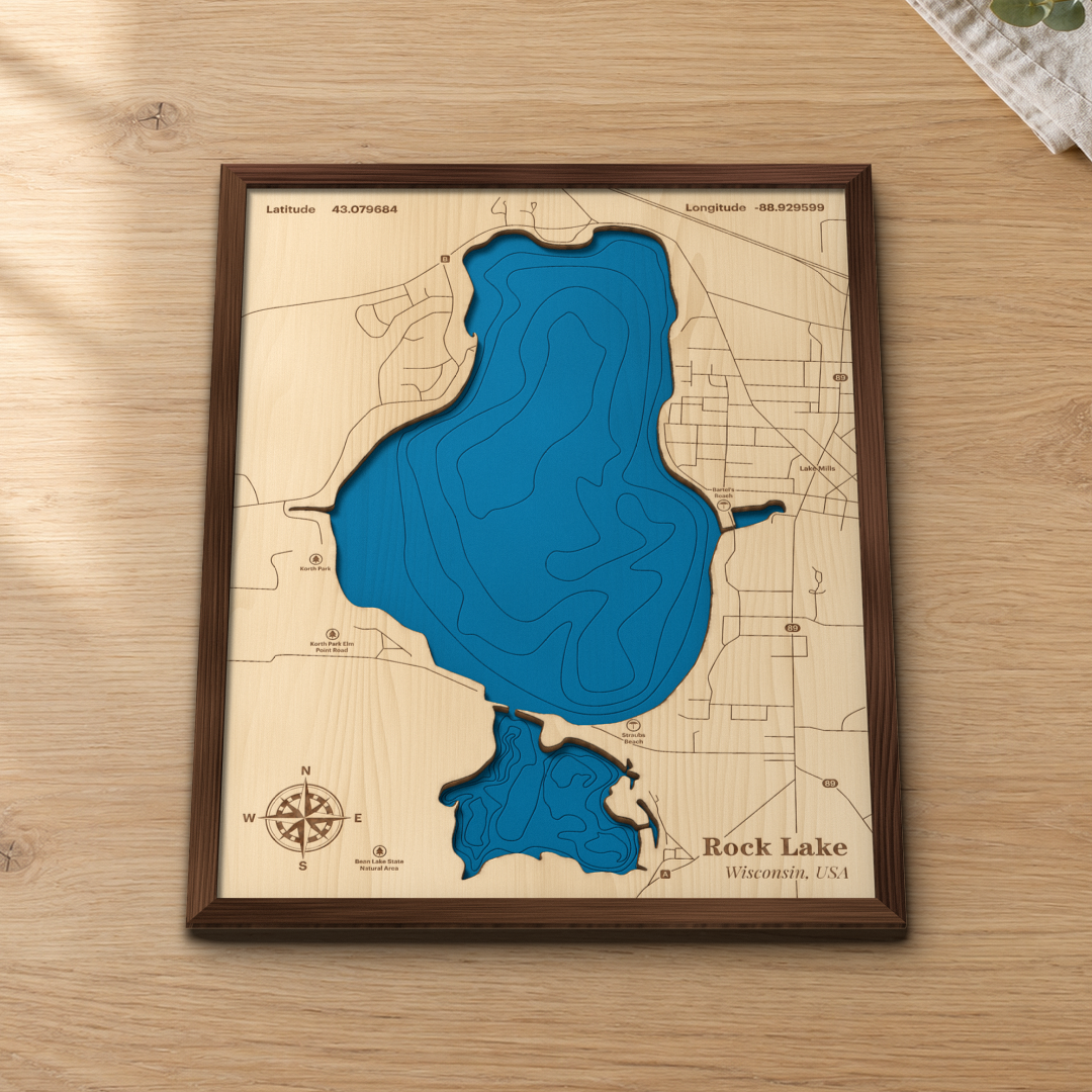Rock Lake wood map lying flat on a wooden tabletop, showing the lake's depth contours with Lake Mills, Korth Park and Bartel's Beach engraved in