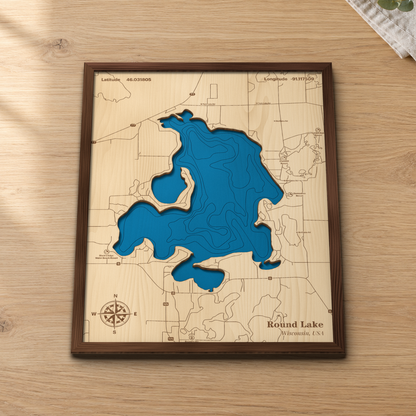 Round Lake wood map lying flat on a wooden tabletop, showing the lake's depth contours with the resorts and lanes around its shoreline engraved in