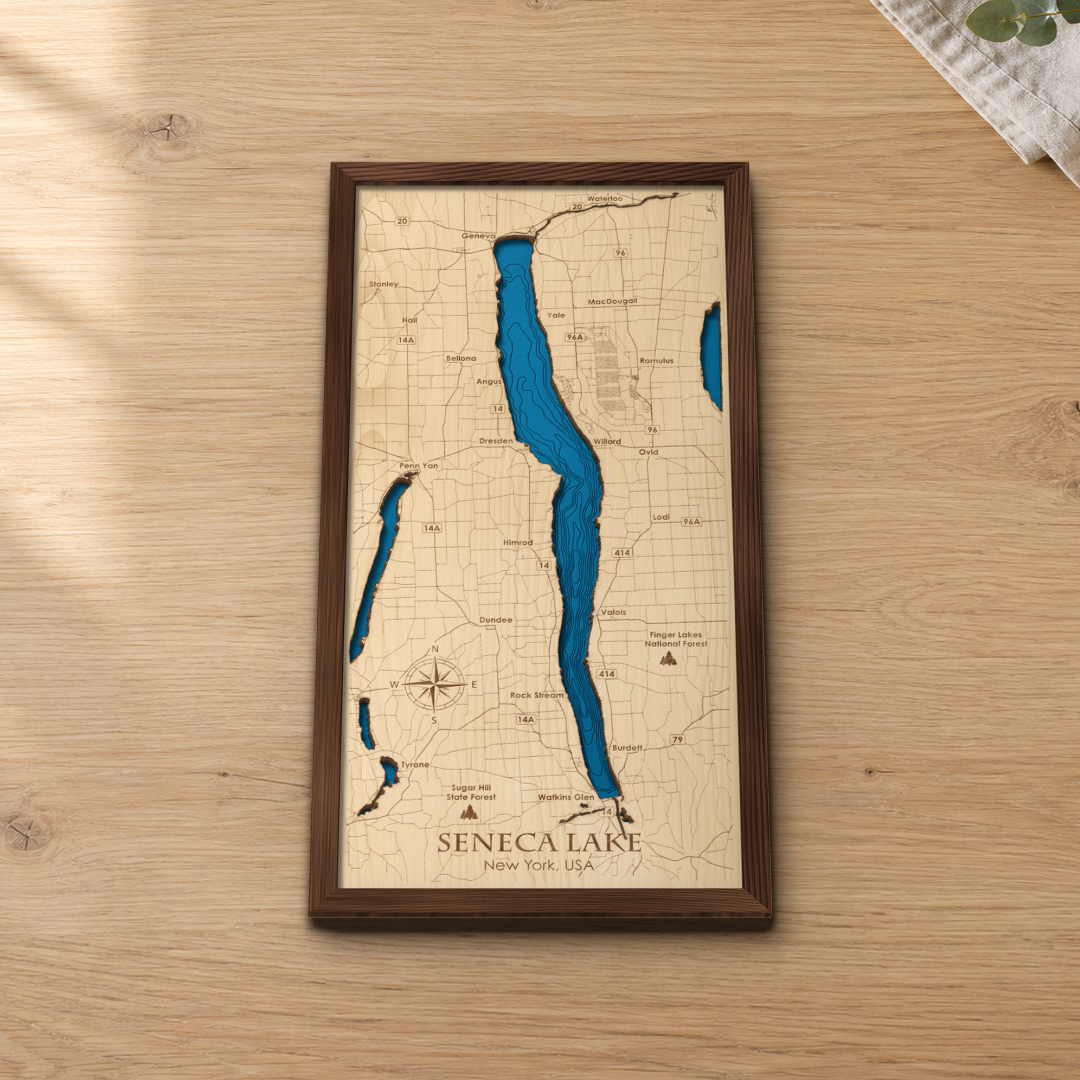 Seneca Lake wood map lying flat on a wooden tabletop, showing the lake's depth contours with engraved towns from Geneva to Watkins Glen
