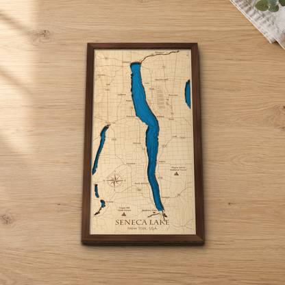 Seneca Lake wood map lying flat on a wooden tabletop, showing the lake's depth contours with engraved towns from Geneva to Watkins Glen