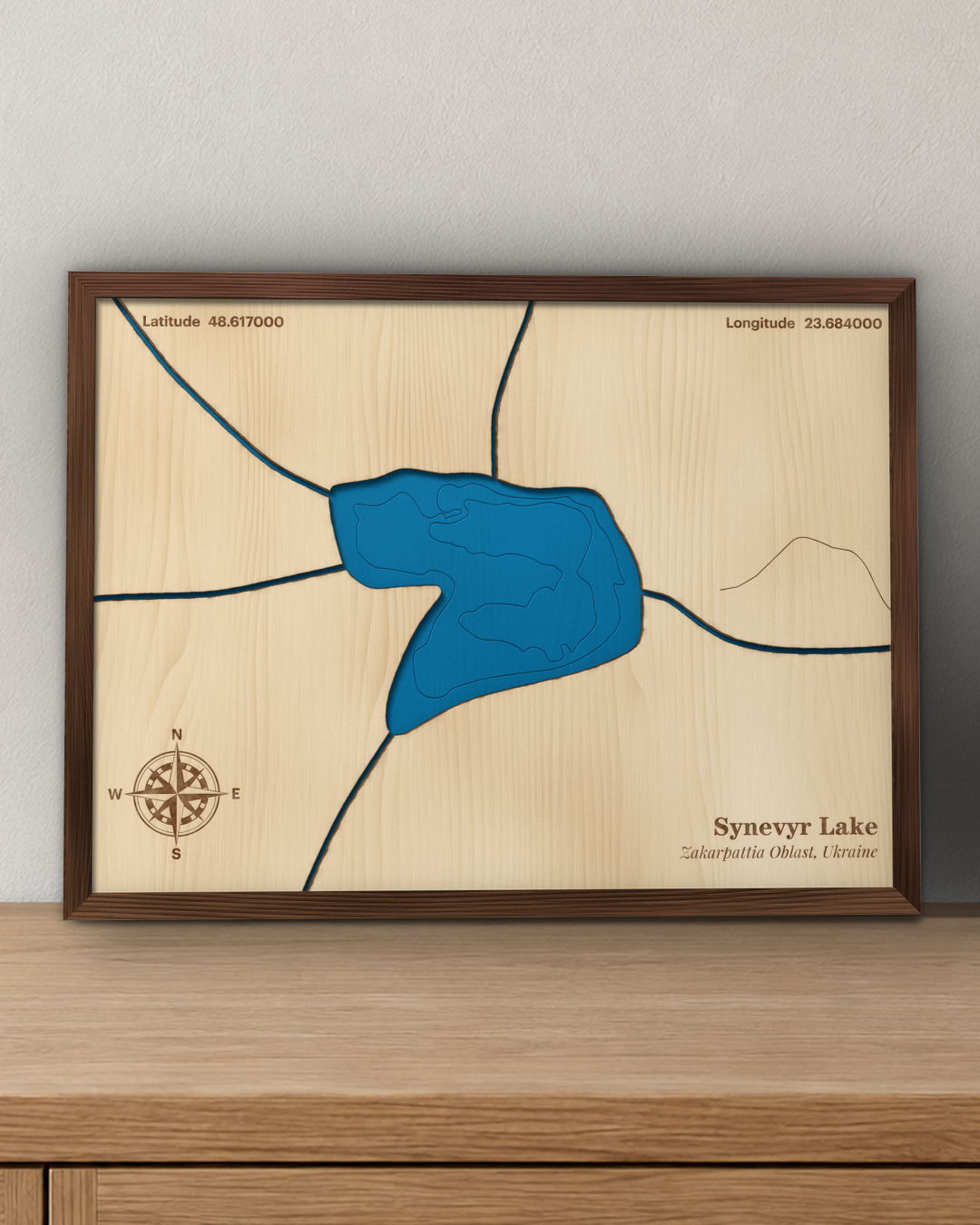 Synevyr Lake wood map in a walnut frame standing on a wooden sideboard against a wall for scale