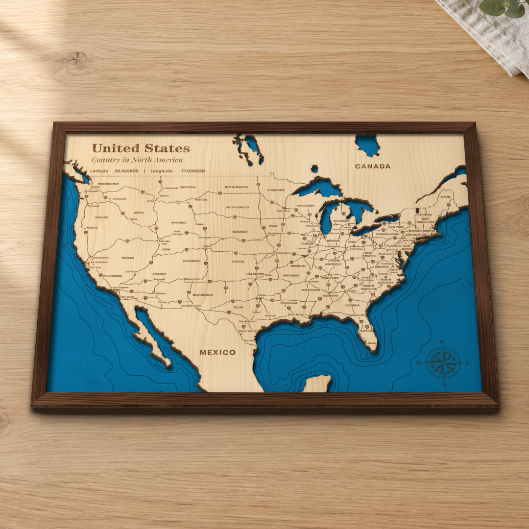 United States wood map lying flat on a wooden tabletop, showing the lower 48 and Great Lakes with engraved states, cities and interstates and ocean depth contours