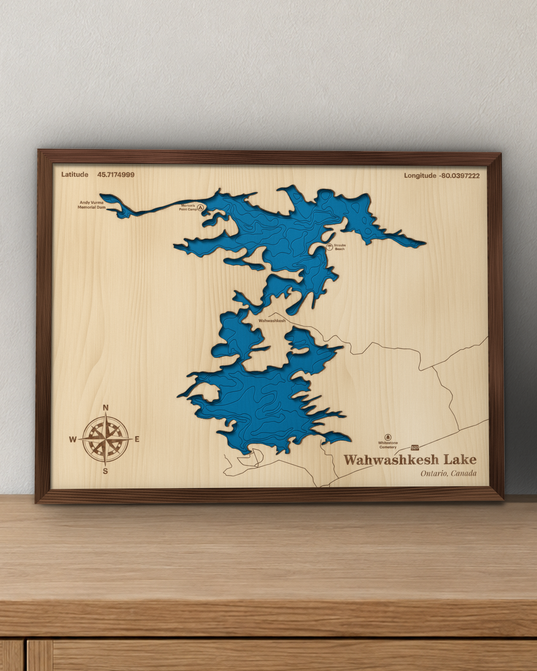 Wahwashkesh Lake wood map in a walnut frame standing on a wooden sideboard against a wall for scale
